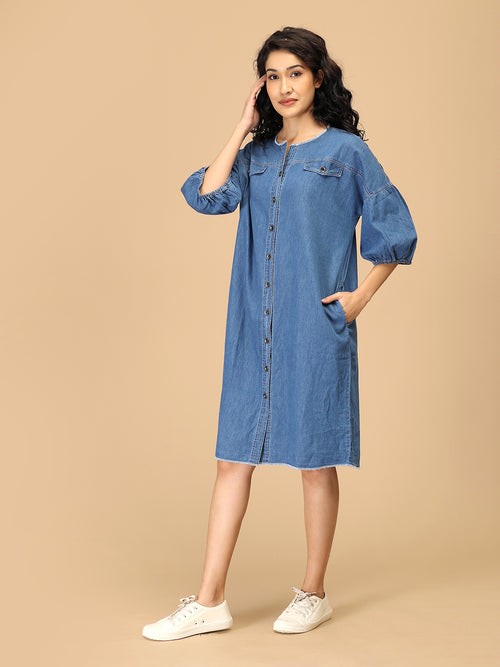 Women’s denim-blue chambray dress with utility pockets and balloon sleeves — side pose.