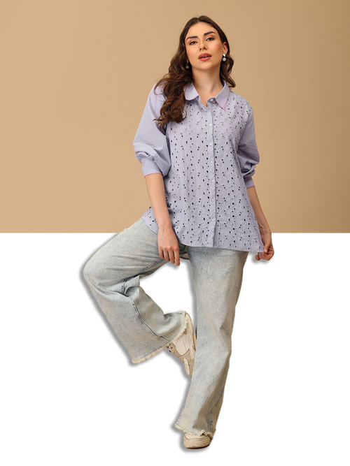 Woman wearing a light purple shirt with a subtle pattern and light blue jeans on a beige background